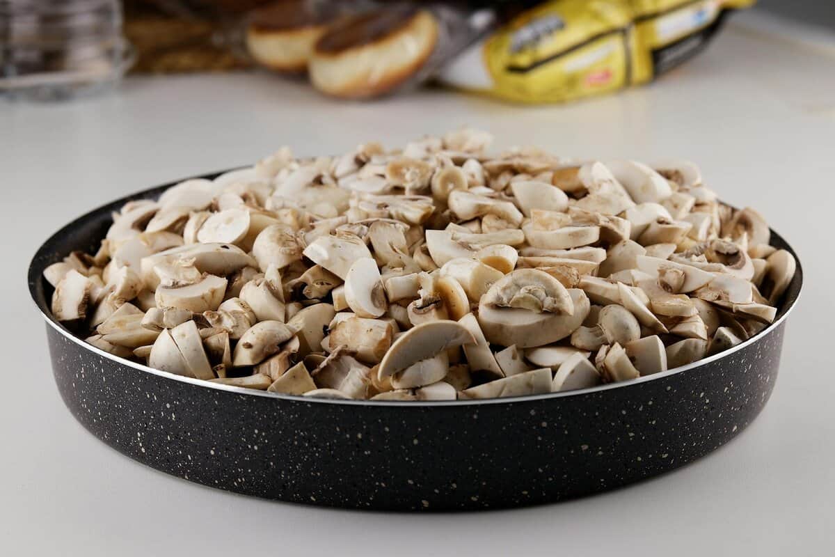 Close-up of sliced mushrooms in a frying pan on a kitchen counter.